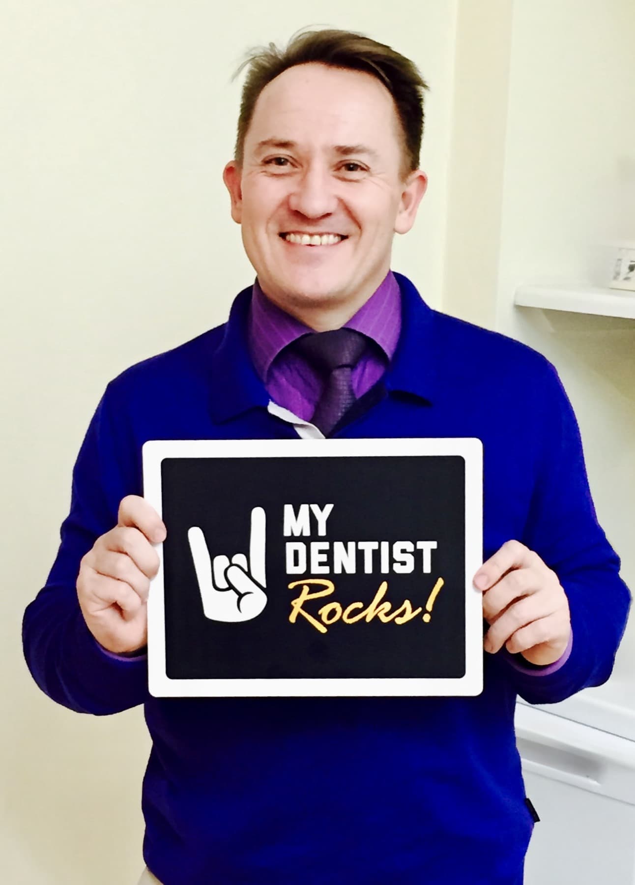 A smiling patient holding a sign praising their dental care